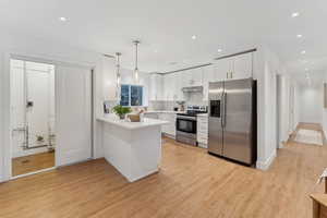 Kitchen featuring appliances with stainless steel finishes, white cabinetry, decorative backsplash, decorative light fixtures, and kitchen peninsula