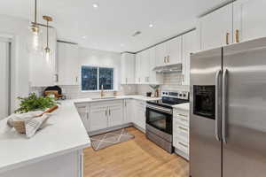 Kitchen with appliances with stainless steel finishes, tasteful backsplash, white cabinetry, sink, and decorative light fixtures