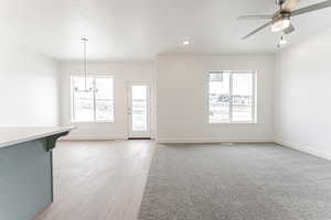 Unfurnished living room featuring light wood-style floors, recessed lighting, ceiling fan with notable chandelier, and baseboards