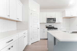 Kitchen with a sink, stainless steel appliances, tasteful backsplash, light countertops, and white cabinets