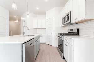 Kitchen with decorative light fixtures, light wood-style floors, appliances with stainless steel finishes, a sink, and a center island with sink