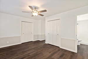 Unfurnished bedroom featuring ceiling fan, connected bathroom, dark hardwood / wood-style floors, and multiple closets