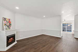 Unfurnished living room with ceiling fan, a textured ceiling, dark hardwood / wood-style flooring, and ornamental molding