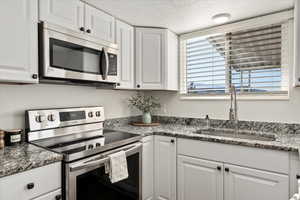 Kitchen with sink, white cabinets, stone countertops, and appliances with stainless steel finishes