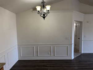 Unfurnished room with dark wood-type flooring, an inviting chandelier, and vaulted ceiling