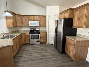 Kitchen featuring vaulted ceiling, hanging light fixtures, sink, dark hardwood / wood-style flooring, and stainless steel appliances