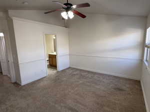 Unfurnished bedroom featuring ceiling fan, light carpet, ensuite bath, and vaulted ceiling