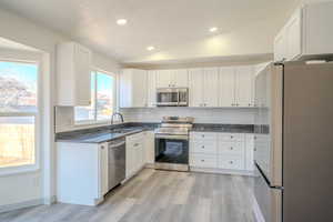 Kitchen featuring vaulted ceiling, white cabinetry, decorative backsplash, sink, and stainless steel appliances