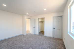 Unfurnished bedroom featuring a spacious closet, light colored carpet, and a closet