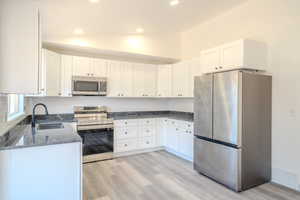 Kitchen featuring dark stone counters, white cabinets, sink, stainless steel appliances, and lofted ceiling