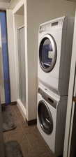 Clothes washing area featuring dark tile patterned floors and stacked washing maching and dryer