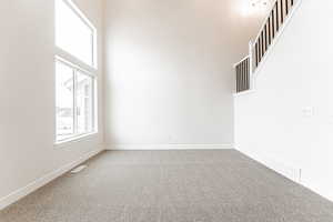 Carpeted empty room featuring baseboards, visible vents, stairs, and a towering ceiling