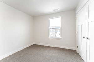 Unfurnished bedroom with carpet, visible vents, a textured ceiling, and baseboards