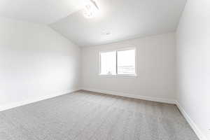 Spare room with light colored carpet, baseboards, visible vents, a textured ceiling, and lofted ceiling