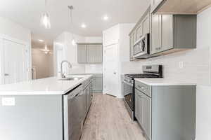 Kitchen with light wood-style flooring, a sink, appliances with stainless steel finishes, and gray cabinets