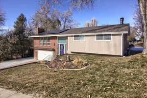 Raised ranch with a garage, solar panels, and a front yard