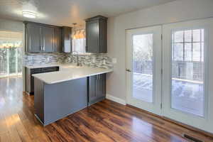 Kitchen featuring hanging light fixtures, decorative backsplash, sink, kitchen peninsula, and dark hardwood / wood-style floors