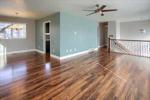 Spare room with ceiling fan with notable chandelier and dark wood-type flooring