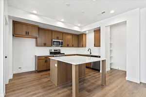 Kitchen with appliances with stainless steel finishes, sink, hardwood / wood-style flooring, light stone counters, and a center island