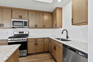 Kitchen with appliances with stainless steel finishes, tasteful backsplash, sink, light stone counters, and dark hardwood / wood-style floors