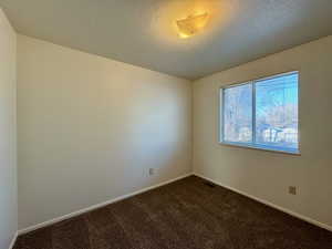 Unfurnished room with dark colored carpet and a textured ceiling