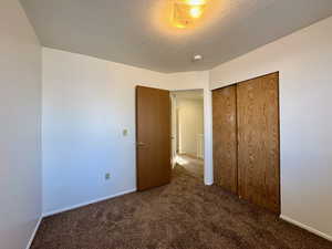 Unfurnished bedroom featuring a textured ceiling, a closet, and dark carpet