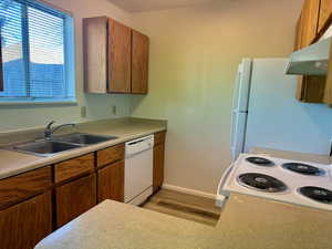 Kitchen with sink, white appliances, light hardwood / wood-style floors, and exhaust hood