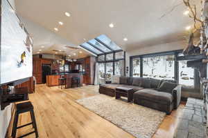 Living room with a skylight, high vaulted ceiling, and light hardwood / wood-style flooring