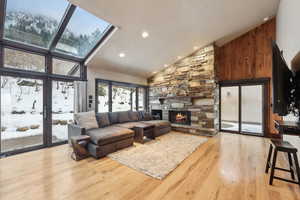 Living room featuring a stone fireplace, light hardwood / wood-style flooring, high vaulted ceiling, and a skylight