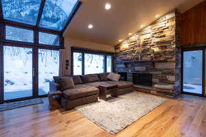 Living room featuring high vaulted ceiling, hardwood / wood-style floors, and a stone fireplace