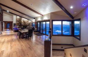 Dining area featuring a stone fireplace, beam ceiling, light hardwood / wood-style floors, and high vaulted ceiling