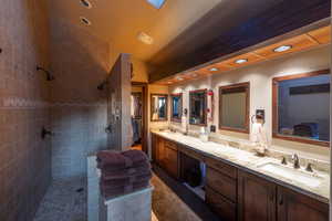 Bathroom featuring vanity, vaulted ceiling, and tiled shower