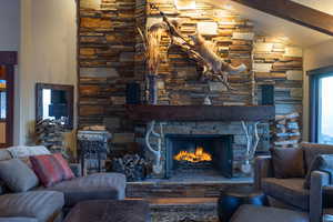 Living room with lofted ceiling with beams and a stone fireplace