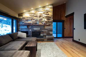 Living room with light hardwood / wood-style flooring, a stone fireplace, and vaulted ceiling