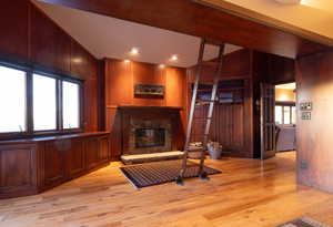 Living room with wooden walls, a stone fireplace, and light wood-type flooring