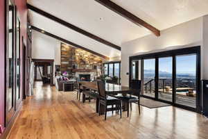Dining room featuring a stone fireplace, high vaulted ceiling, beamed ceiling, light hardwood / wood-style floors, and a textured ceiling