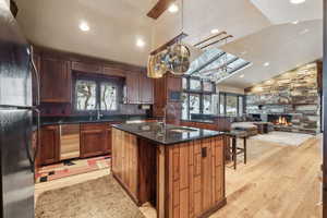 Kitchen featuring black refrigerator, lofted ceiling with skylight, a kitchen island with sink, and sink