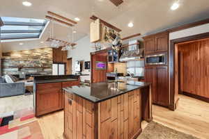 Kitchen with tasteful backsplash, decorative light fixtures, light wood-type flooring, stainless steel microwave, and a kitchen island with sink