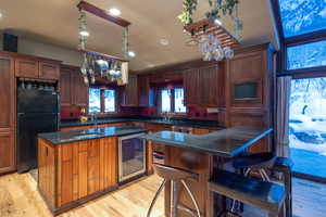 Kitchen with black refrigerator, light hardwood / wood-style floors, sink, a kitchen island, and beverage cooler