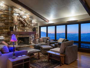 Living room with a textured ceiling, wood-type flooring, a stone fireplace, lofted ceiling with beams, and a mountain view