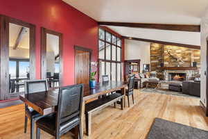 Dining space featuring beam ceiling, wood-type flooring, high vaulted ceiling, and a fireplace