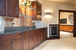 Kitchen with wooden walls, light carpet, sink, dark stone counters, and beverage cooler