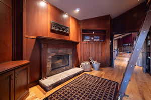 Living room with light wood-type flooring, wooden walls, a fireplace, and lofted ceiling