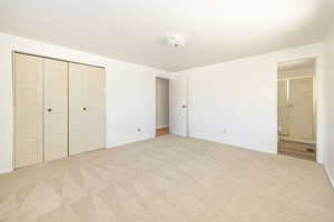 Unfurnished bedroom featuring light colored carpet, ensuite bathroom, and a closet