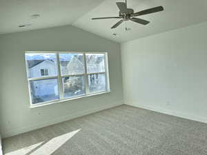 Carpeted empty room featuring ceiling fan, vaulted ceiling, and a wealth of natural light