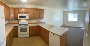 Kitchen featuring white appliances, decorative light fixtures, sink, kitchen peninsula, and light colored carpet