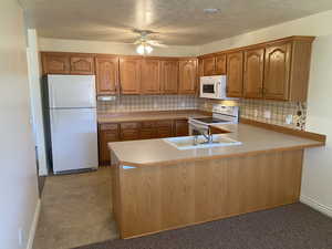 Kitchen with decorative backsplash, sink, white appliances, and kitchen peninsula