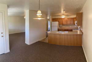 Kitchen with range, hanging light fixtures, sink, dark colored carpet, and white refrigerator