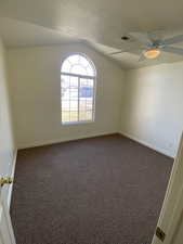 Second bedroom with a textured ceiling, vaulted ceiling, and ceiling fan