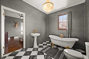 Bathroom with ceiling fan with notable chandelier, a tub to relax in, and toilet